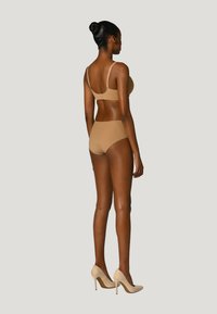 Bh und Unterhose in Nude-Farbe. Weicher Stoff mit glatter Textur, verstellbare Träger und minimale Beschläge. High Heels in Beige.