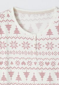 Camisa blanca con cuello redondo, con patrones en píxeles rojos de árboles, copos de nieve y corazones. Tiene una tapeta de cuatro botones en el centro frontal.