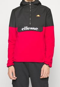 Sudadera polar roja y negra con cremallera hasta el pecho y capucha, con un bolsillo frontal y el logo "ellesse" en el pecho. Textura suave, ajuste casual.