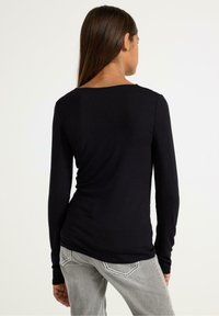 Sort langærmet top med scoop halsudskæring, der har en tætsiddende pasform og blød tekstur. Sammen med grå jeans, der viser bagfra.