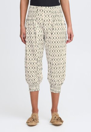 Pantalons légers de couleur crème avec des motifs fléchés verticaux noirs. Présentent des ourlets de cheville élastiqués pour un ajustement décontracté. Texture douce.