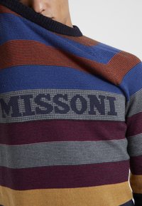 Gebreide trui met blauwe, rode, grijze en gele strepen. Voorzien van een ronde halslijn en het "MISSONI"-logo in donkergrijs op de borst.