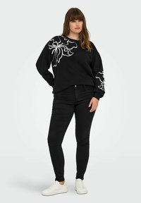 Black sweatshirt with white floral design on one sleeve, paired with black jeans and white sneakers. Soft fabric, relaxed fit, and long sleeves.