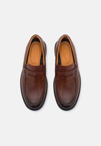 Mocasines de cuero marrón con un acabado pulido, que presentan un diseño cosido y acentos sutiles sobre una plantilla acolchada y una punta redondeada.