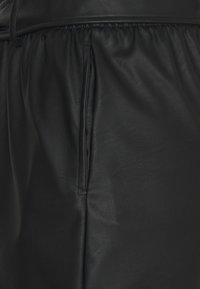 Shorts en cuir noir avec une taille froncée et des poches latérales. La texture est lisse avec des détails de grain subtils.
