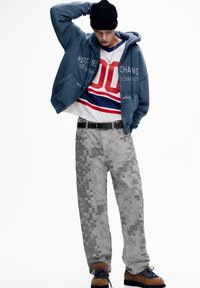 Felpa blu con scritta, t-shirt a righe rosse e blu, pantaloni grigi pixelati e scarpe marroni pelose con lacci blu. Look casual da strada.