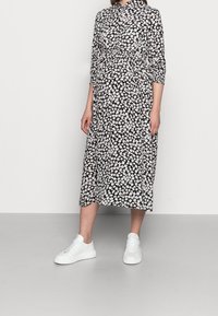 Robe florale noire avec des fleurs blanches et roses, dotée d'un col, de manches longues et d'une taille froncée, associée à des baskets blanches.