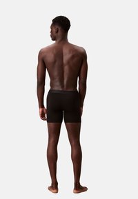 Czarnie bokserki wykonane z gładkiego materiału, dopasowany krój, długość do połowy uda, z miękką elastyczną talią, model widziany z tyłu.