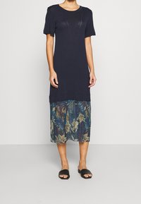 Granatowa sukienka krótki rękaw z warstwowym, półprzezroczystym kwiatowym dołem. Posiada fakturowany materiał, okrągły dekolt i luźny krój. Czarne płaskie sandały.