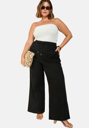 Schwarze Hosen mit weitem Bein und verstellbarem Kordelzugbund, kombiniert mit einem weißen trägerlosen Oberteil. Als Accessoires dienen eine strukturierte beige Clutch und Sonnenbrillen.