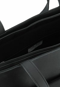Sac à main en cuir noir avec fermeture éclair, présentant un extérieur lisse et un intérieur spacieux et doublé avec une étiquette. Deux poignées pour le transport.