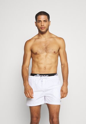 White swim shorts with a black elastic waistband featuring "ellesse" logo. Lightweight fabric, drawstring closure, and short cut.