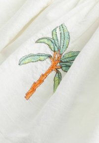 Vyšívaná látka s dizajnom palmy so zelenými listami a oranžovým kmeňom na bielom, textúrovanom pozadí.