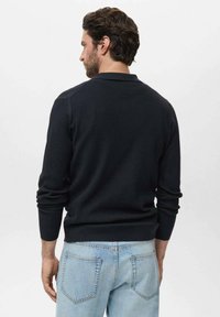 Suéter negro de canalé con cuello redondo, mangas largas y dobladillo ajustado; combinado con unos vaqueros de mezclilla azul claro.