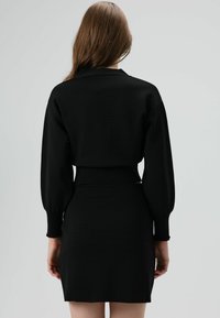 Schwarzes gestricktes Kleid mit tailliertem Schnitt, langen Puffärmeln und gerippter Struktur. Rückansicht zeigt glatten Stoff und schlichtes Design.