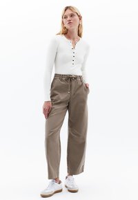 Witte langesleeve top met knoopsluiting, gecombineerd met losse, beige utility pants en witte sneakers met tan accenten.