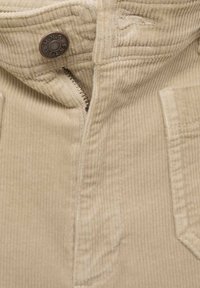 Beige corduroy fabric with a zip closure, button detail, and two front pockets. The texture features vertical lines in the fabric.
