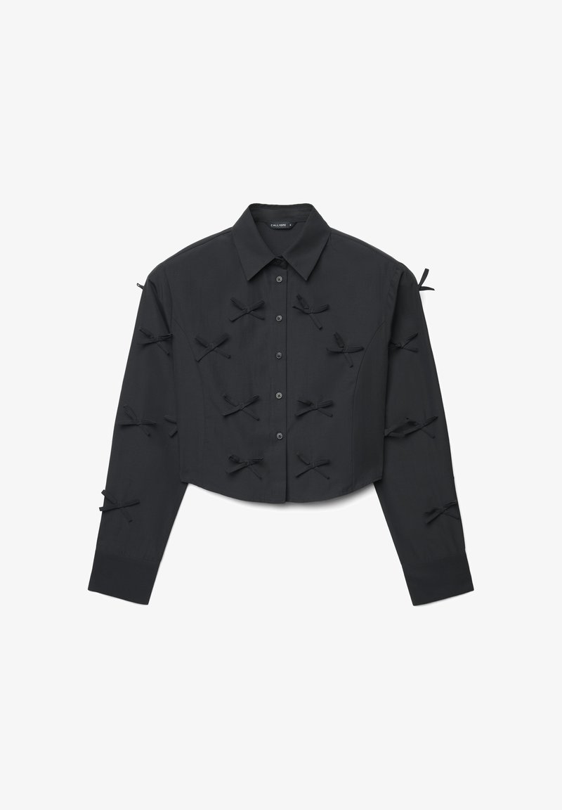 Schwarzes, kurzes Langarmshirt mit Knopfleiste vorne und mehreren kleinen Stoffschleifen, die über Vorderseite und Ärmel verteilt aufgenäht sind.