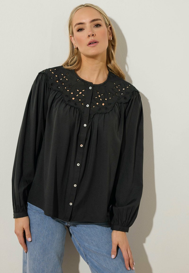 Svart blus med en dekorerad broderad ok, långa ärmar och knäppning fram. Slätt tyg och avslappnad passform.