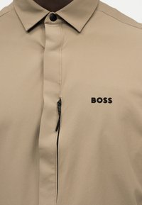 Μπεζ πουκάμισο με γιακά, κρυφό φερμουάρ και μαύρο λογότυπο "BOSS" στο αριστερό στήθος.