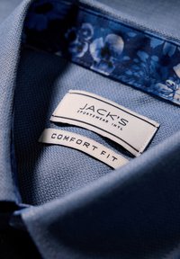 Sininen kauluspaita, jossa on teksturoitu kangas. Kukallinen printti kauluksen sisäpuolella. Tunnuksessa lukee "JACK'S" ja "COMFORT FIT."