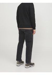 Felpa nera, maglietta beige sotto, jeans grigi scuri e sneaker grigi. Presenta cuciture visibili e una silhouette dalla vestibilità rilassata.