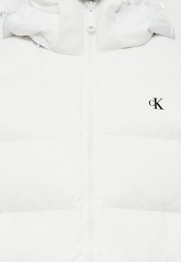 Witte pufferjack met capuchon, centrale rits en zwart "cK" logo op de linkerborst.