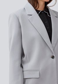 Light gray blazer with a structured design, notched lapels, single button closure, and a front pocket. Made of smooth fabric.