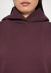 Felpa maroon con colletto alto e cappuccio a doppio strato. Realizzata in tessuto morbido, presenta un finish testurizzato e polsini a costine.