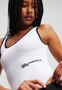 Fehér bordázott ujjatlan felső fekete díszítéssel. A "KARL LAGERFELD JEANS" szöveg fekete hímzéssel van ellátva. Testhez simuló fazon, kerek nyakkivágással.