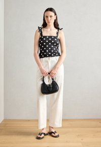 Top cu buline negre și cu legături pe umeri, pantaloni largi albi, o geantă mică neagră și sandale plate negre, toate amplasate pe un podea din lemn.