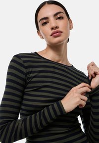 T-shirt à manches longues avec des rayures horizontales vert olive et bleu marine, en tissu doux, à encolure dégagée et à coupe ajustée.