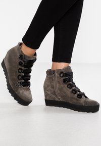 Sneakers wedge in suede grigio con lacci neri in raso, occhielli circolari e dettaglio con zip laterale; superficie texturizzata e suola in gomma.
