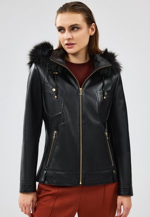 Black leather jacket with a faux fur hood. Features zippered front, angled chest pockets, and gold accents. Smooth texture and tailored fit.