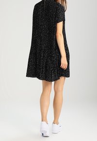 Vestido negro con mangas cortas, patrón de puntos blancos dispersos, falda plisada y un ajuste relajado. Combinado con zapatillas blancas para crear contraste.