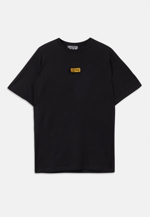 T-shirt noir à manches courtes avec un petit patch rectangulaire jaune du logo Versace Jeans Couture centré sur la poitrine.