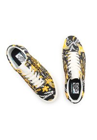 Une paire de baskets Vans noires et jaunes à motifs floraux avec des lacets et des semelles blanches, vue de dessus sur un fond blanc.