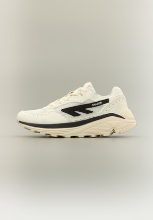 Weißer Sportschuh mit schwarzen Akzenten, strukturiertem Obermaterial und gepolsterter Sohle. Mit einem Logo und gemusterten Details an der Seite.