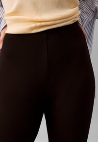 Svarte leggings laget av elastisk materiale, med høy midje og glatt tekstur. Brukes med en ribbestrikket lys gul topp og blå stripete skjorte.