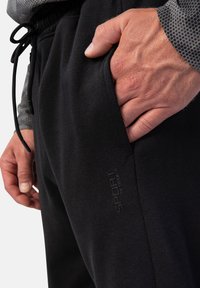 Schwarze Sweatpants mit glatter Textur, elastischem Bund und einer Seitentasche. Mit dezentem Logo-Detailing am Oberschenkel.