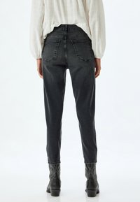 Jeans de denim negros de altura alta con un ajuste tapered, que presentan bolsillos traseros y un ligero desgaste. Combinados con botas de tobillo negras con estampado en relieve.