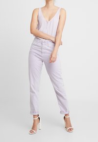 Lavender sleeveless top with buttons, paired with light lavender cuffed jeans and white heeled sandals, against a plain background.