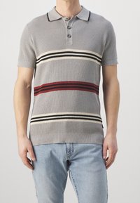 Camisa polo de punto gris con mangas cortas, tres botones y rayas horizontales en rojo, negro y crema. Cuello y dobladillo acanalados.