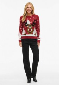 Punane pühade sviiter, mis on kaunistatud suure põhjapõdraga, kellel on sarved, ümbritsetud valgetest puudest ja lumehelvestest. Kombineeritud mustade pükstega.