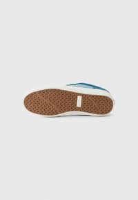 Sneaker sole with a textured brown rubber surface, featuring a white edge and geometric patterns, designed for traction and durability.