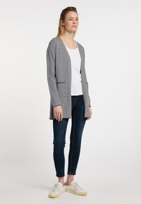 Randig cardigan i svart och vitt, öppen framsidan design, långa ärmar, tillverkad av ett mjukt material, i kombination med en vit topp och mörka jeans.