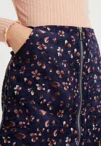 Navyblå kordkjol med rosa blommönster, med sidofickor och dragkedjestängning. Mjuk textur och uppbyggd design.