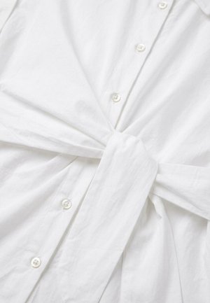 White button-up shirt with a fabric belt tied in a knot at the waist, showing slight wrinkles in the fabric.