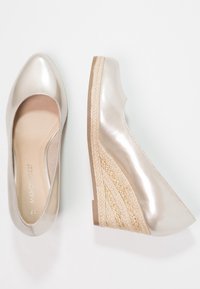 Des chaussures compensées beige métallisé avec un dessus lisse, un bout arrondi et une semelle intermédiaire texturée en corde. Présente un petit talon compensé pour un peu de hauteur.