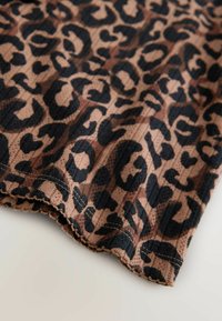 Lähedane vaade pruunile kangale musta leopardimustriga, millel on ribakujuline tekstuur ja tikitud laineline äär.